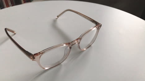 Modern-eyeglasses-in-light-colour-lie-on-a-white-table,-bright-glasses-frame,-slow-motion-footage