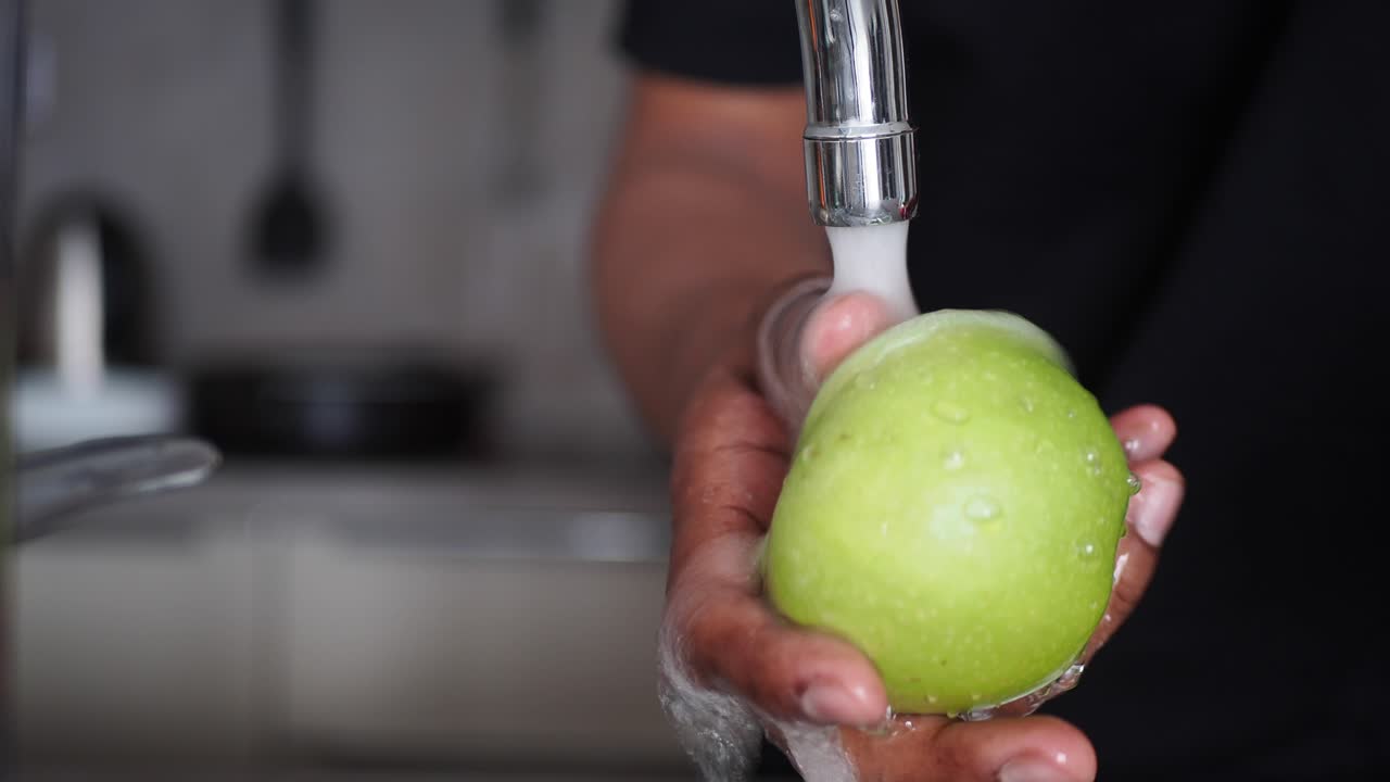lavando una manzana verde bajo un grifo