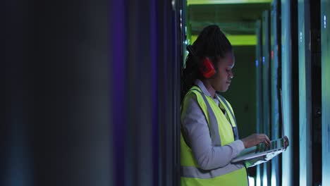 técnica informática afroamericana que usa una computadora portátil trabajando en la sala de servidores de negocios