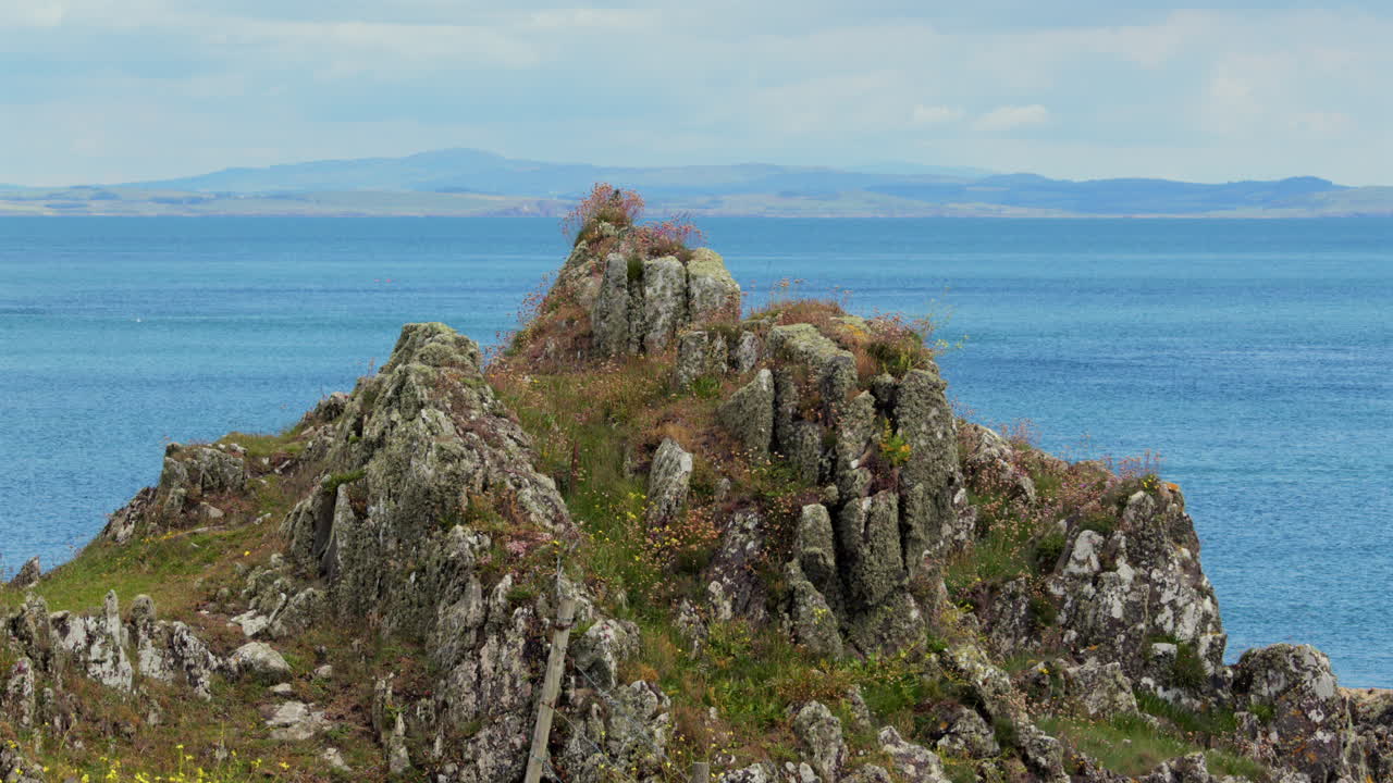 Shot of grass covered rocks with the Mull of Galloway in background. Isle head, Isle of Whithorn