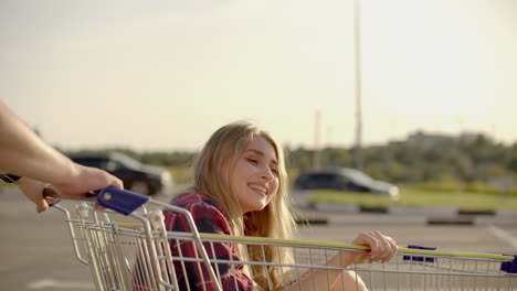 una joven pareja romántica se está divirtiendo con el carrito del supermercado por la noche. un hermoso hombre barbudo y una joven atractiva están pasando tiempo juntos al aire libre.