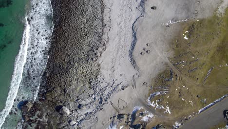 Aerial-birdseye-view-of-Uttakleiv-beach-in-Lofoten-Norway-in-late-winter-with-some-light-snow-on-the-ground,-crashign-waves-and-a-heart-someone-drew-in-the-sand