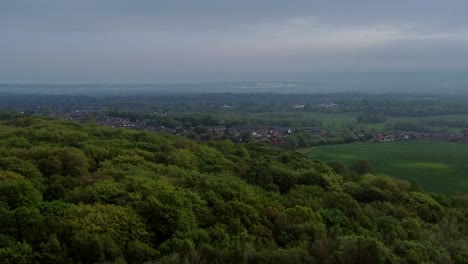 Flying-over-woodland-trees-overlooking-vast-Lancashire-countryside-farmland-on-hazy-morning-aerial-view