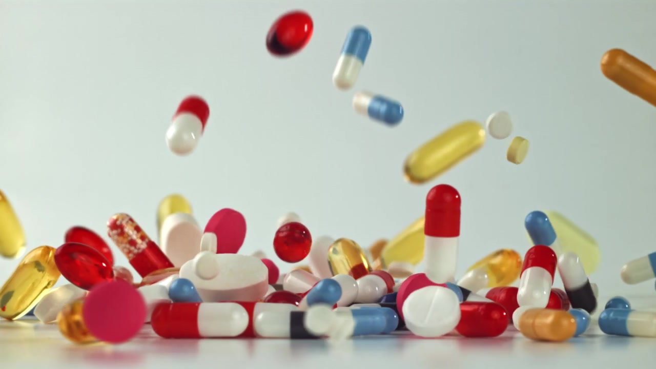 Colorful Pills and Capsules Falling in Slow Motion onto White Surface