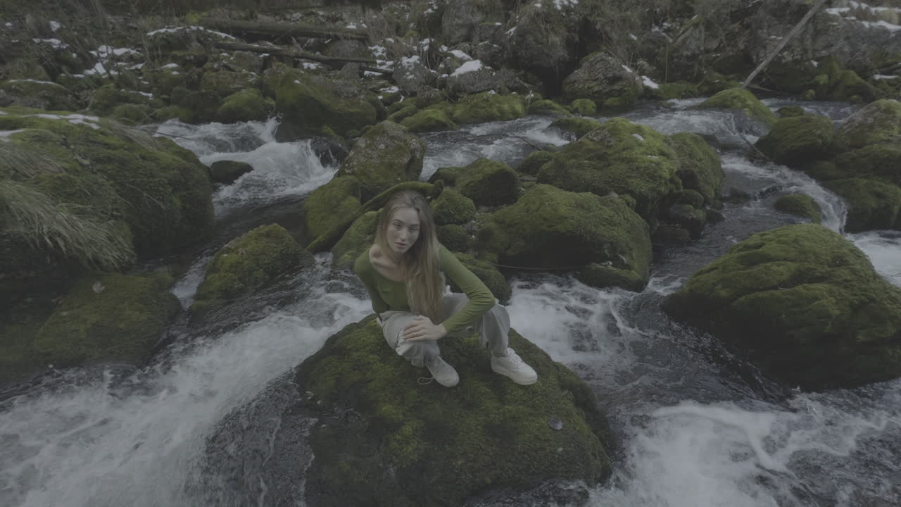 Woman Sitting on a Mossy Rock in a Winter Stream