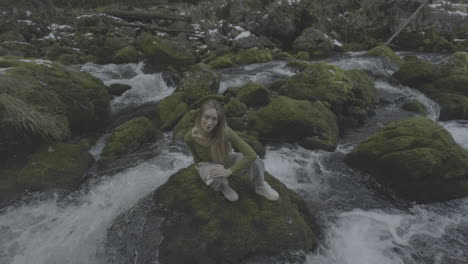 woman sitting on a mossy rock in a winter stream