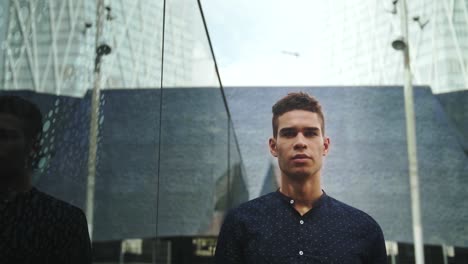 well-dressed entrepreneur businessman portrait of a young attractive trendy man looking into his own reflection on a building window on a sunny day with a modern urban city background in slow motion