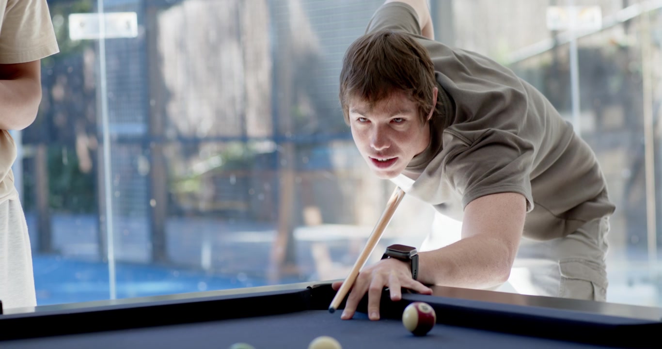 Adult male friends playing pool main player taking shot lining and striking cue at scattered balls