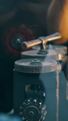 cu: professional jeweler turns handle of forge-rolling machine working with long gold metal wire in workshop closeup