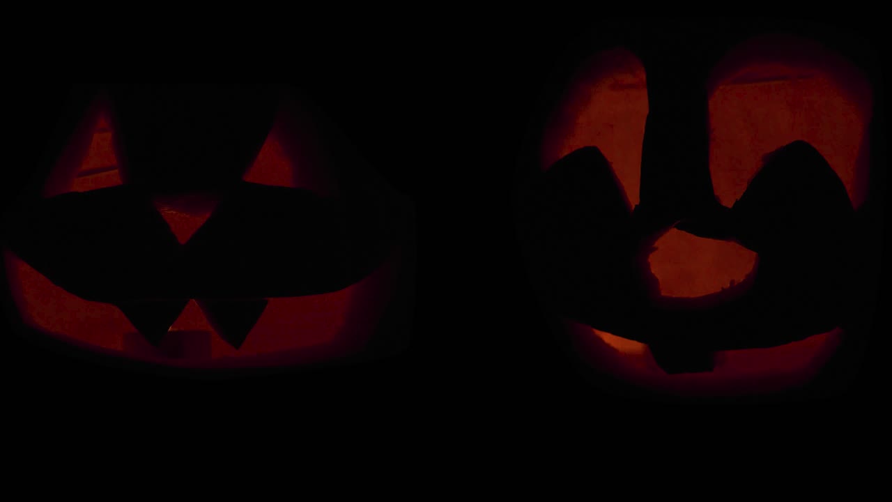 Happy Halloween 2 Jack O' Lanterns glowing in the dark wishing Happy Halloween: carved Pumpkin decorations with burning candles inside.
