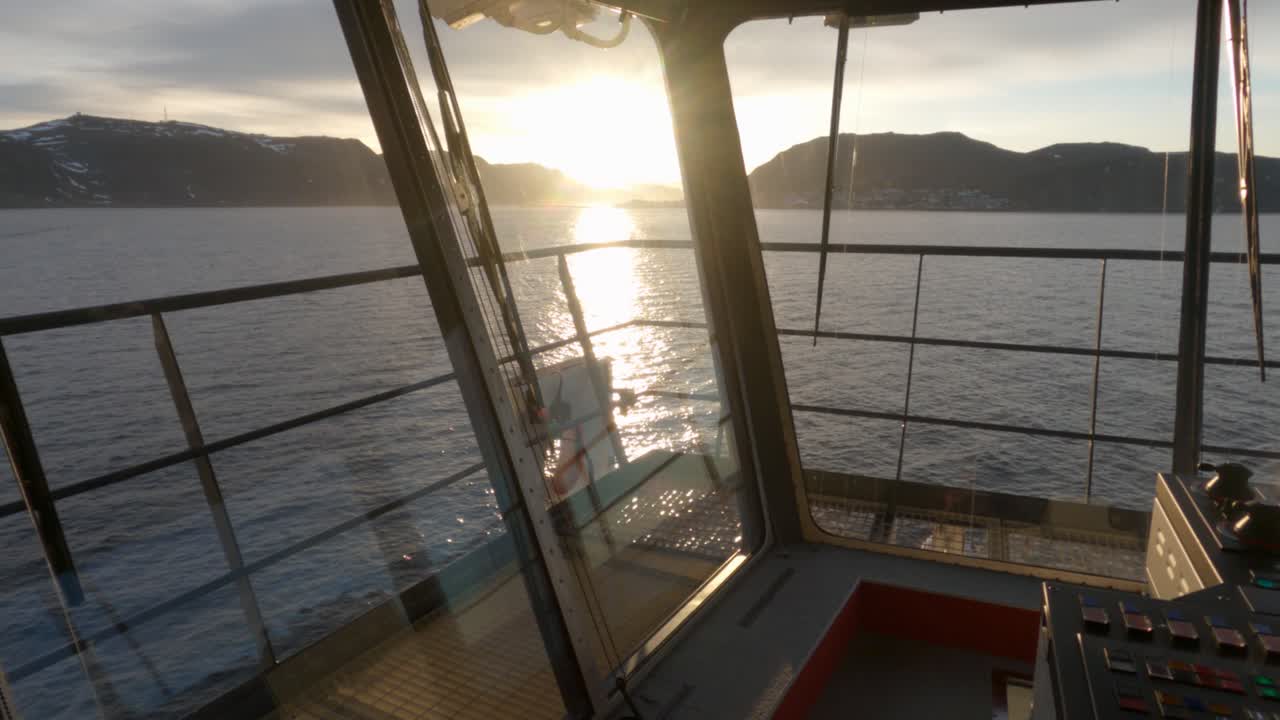 Blick vom Brückendeck eines Kreuzfahrtschiffes während der Mitternachtssonne am Nordkap, Norwegen. Goldenes arktisches Licht spiegelt sich in ruhigen Fjordgewässern, umgeben von dramatischen Bergsilhouetten.