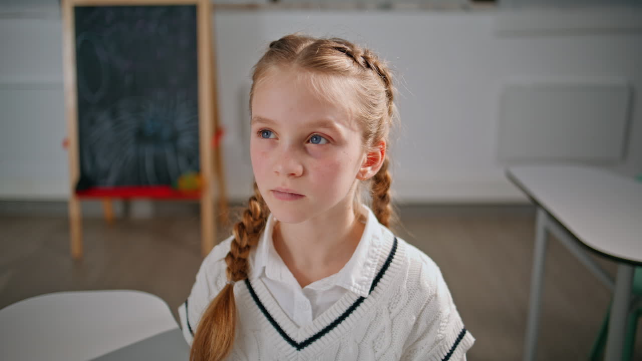 Attentive schoolgirl listening questions from teacher in classroom closeup