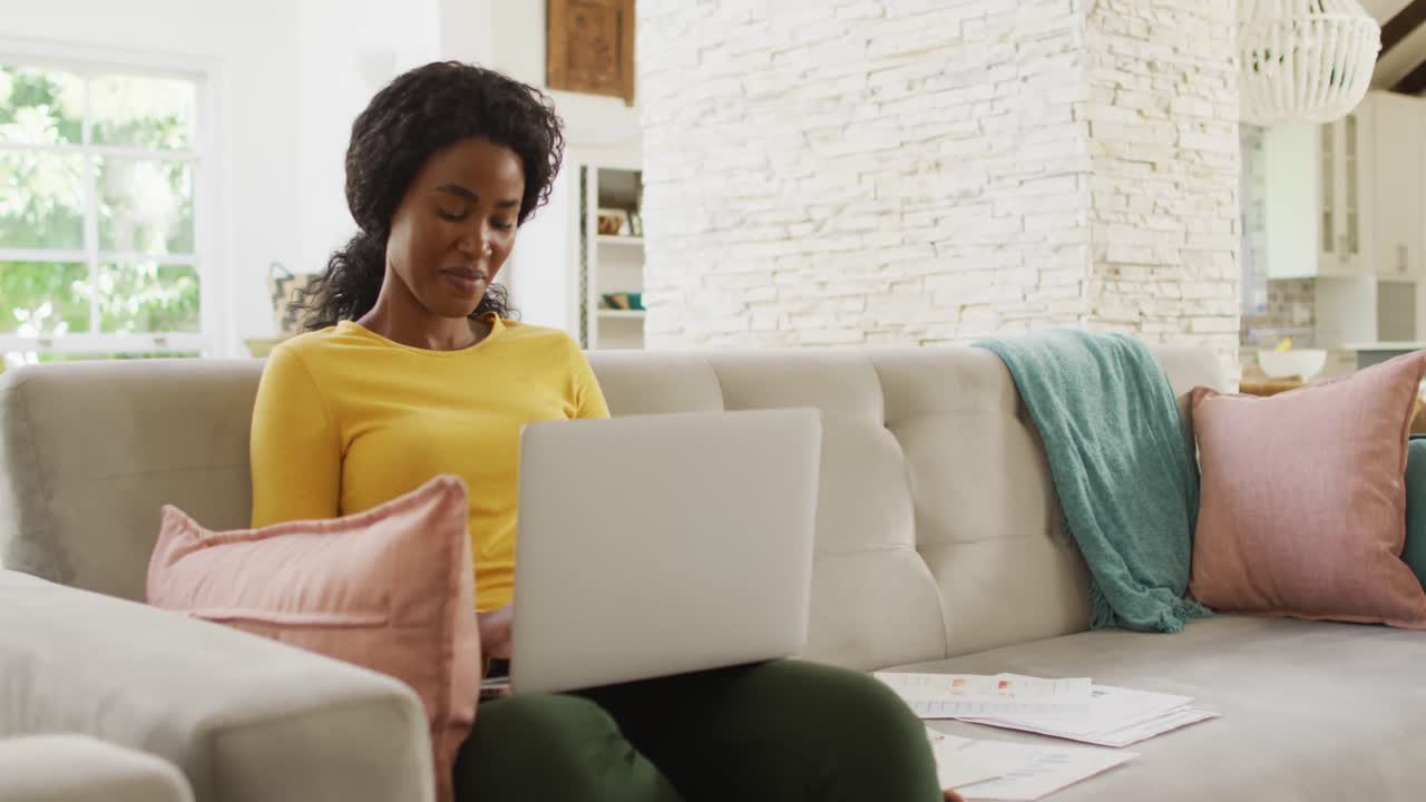 Video of happy african american woman on sofa using laptop