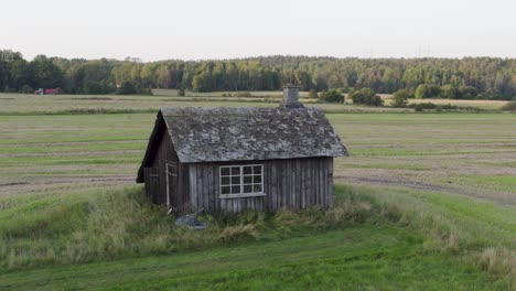 old wooden blacksmith shop with worn roof in open fields of dalsland in sweden. orbiting drone shot