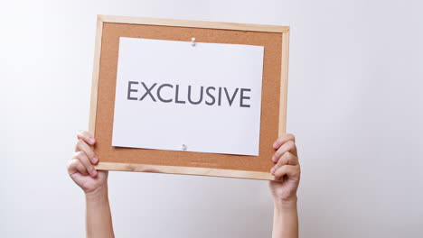 Woman's-hand-shows-the-paper-on-board-with-the-word-EXCLUSIVE-in-white-studio-background-with-copy-space