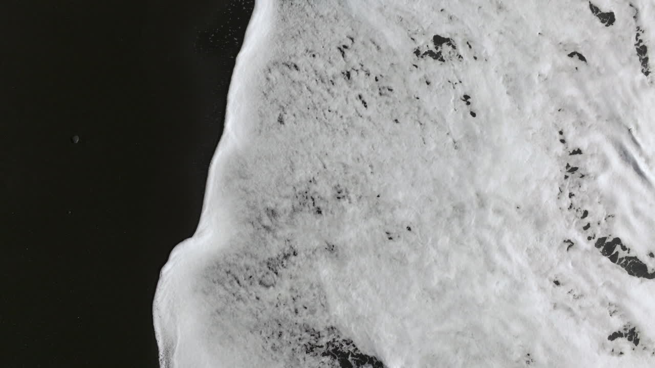 las olas espumosas que se arrastran sobre la playa de arena negra de reynisfjara en vik, islandia