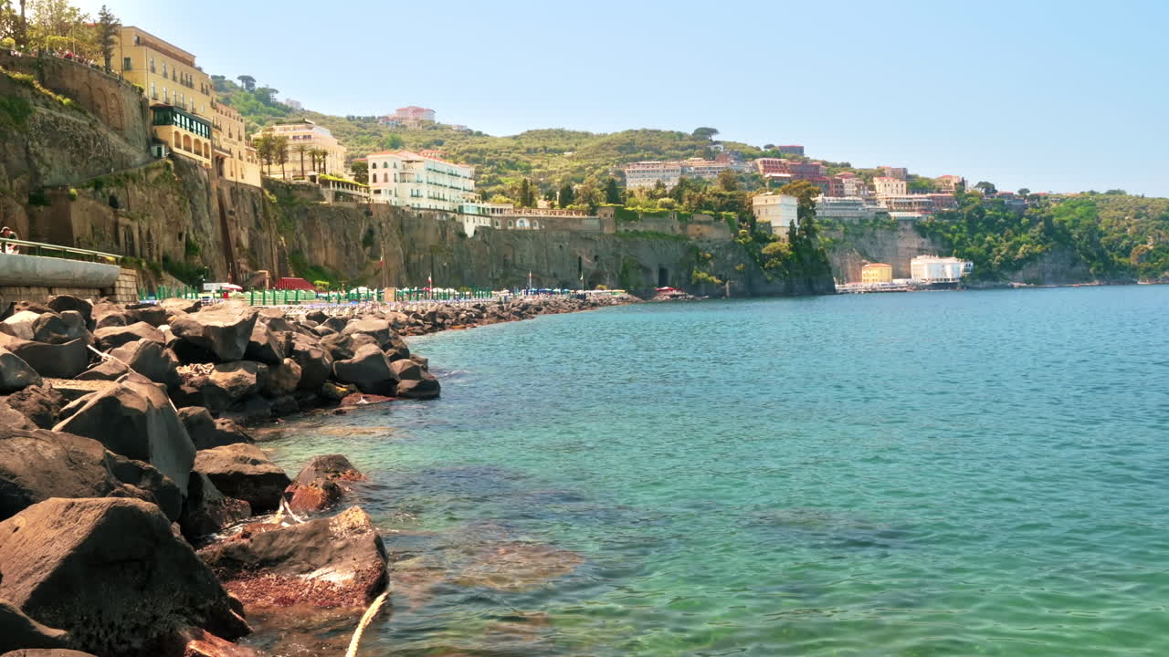 Vista della costa tirrenica a Sorrento, Italia. Pontili con lettini per il riposo, acqua trasparente, scogliere con edifici