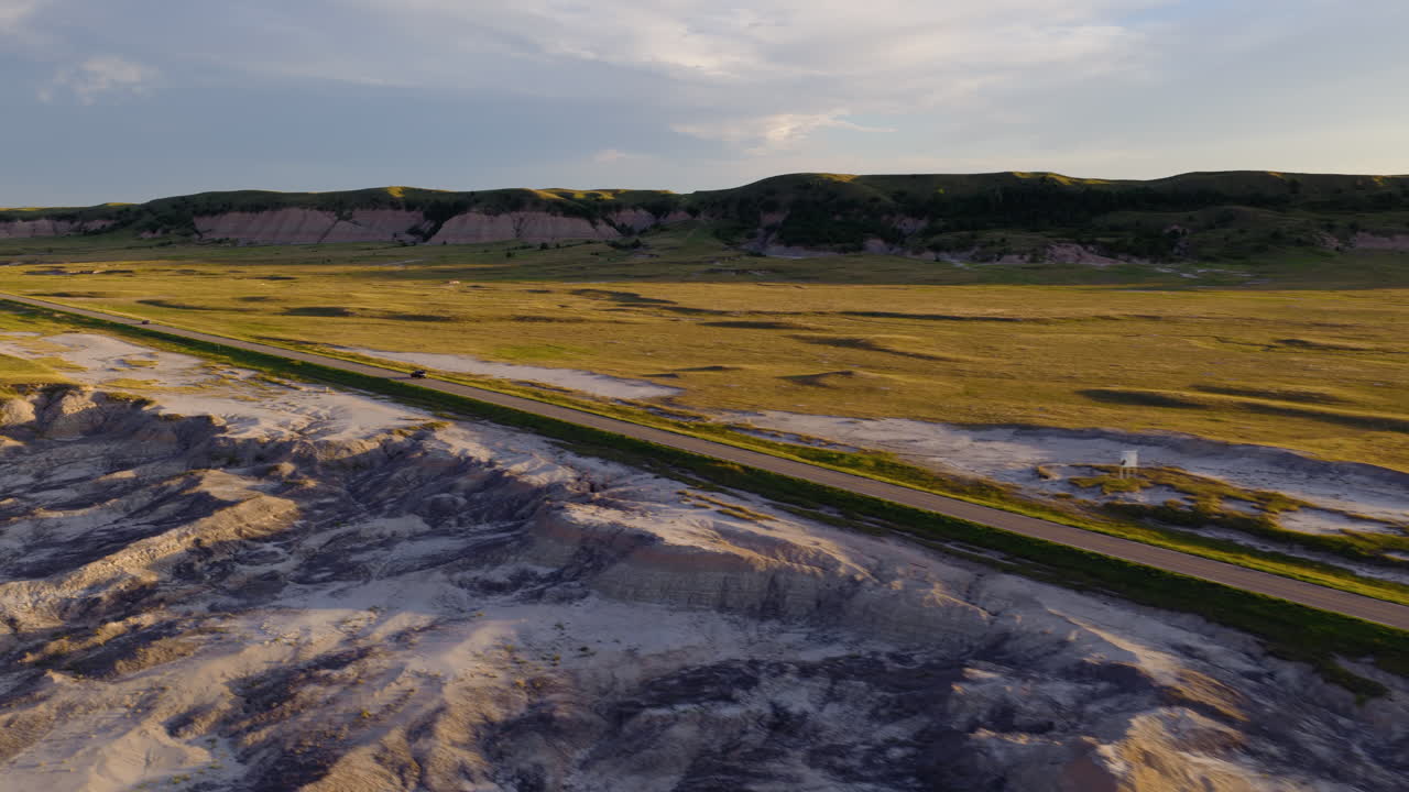 Lonely Road Carving Across Harsh Badlands at Golden Hour by Drone