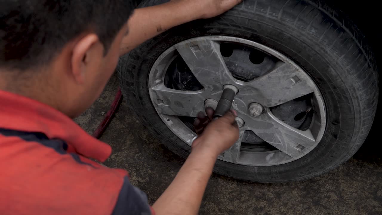 Young Latino Brown expert mechanic manually tightening wheel lug nuts with tools in latinamerican car garage