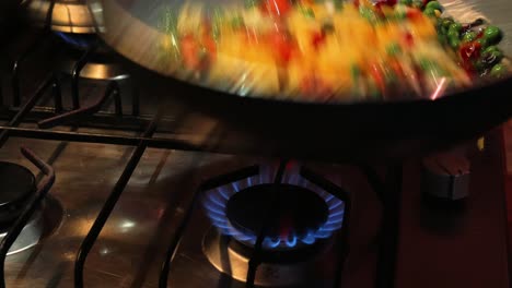 chef is tilting and overturning vegetables on a hot frying pan