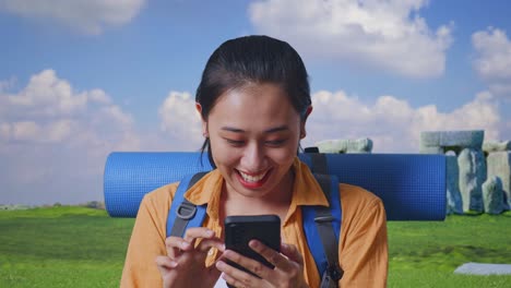 Close Up Of Asian Female Hiker With Mountaineering Backpack Looking At The Smartphone And Saying Wow While Traveling In Stonehenge
