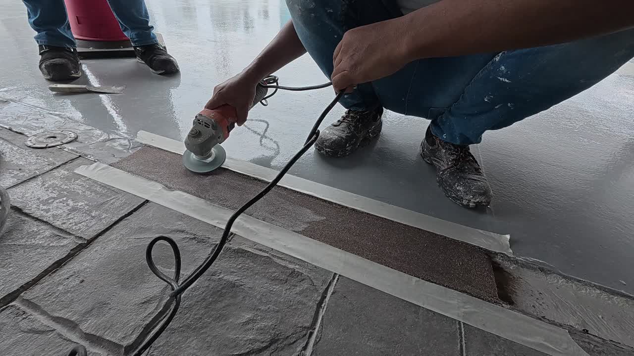 Uneven concrete patching is being ground smooth by a construction worker using an electric grinder. Safety is the top priority for this meticulous work.