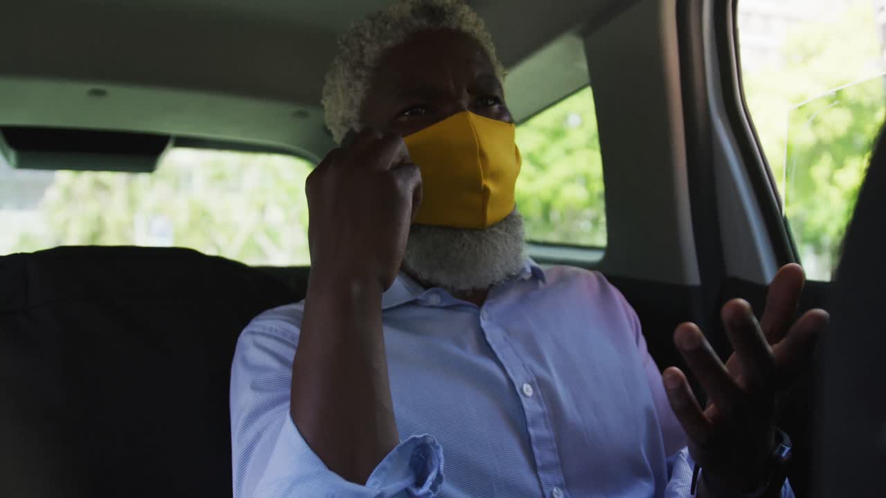 En ældre afroamerikansk mand med ansigtsmaske taler i smartphone, mens han sidder i bilen.