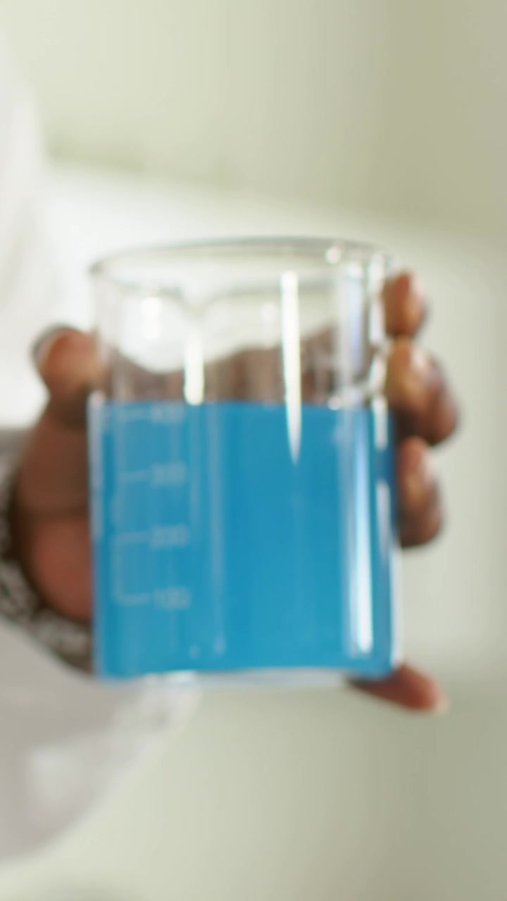 Video verticale: Tecnico di laboratorio che dimostra stabilizzando un becher graduato, mostrando liquido blu, camice bianco