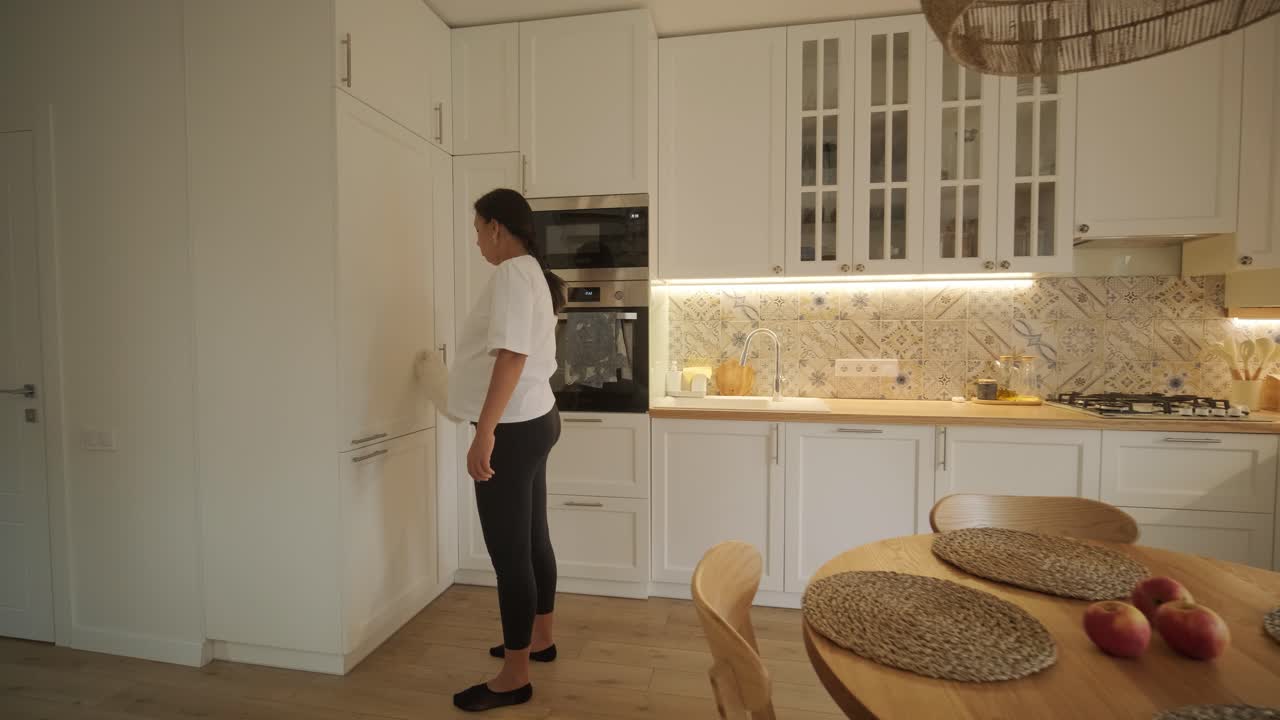 Una bella donna incinta che riordina la sua casa, impegnata nelle faccende domestiche. La scena cattura la vita domestica, la maternità e l'equilibrio tra routine e preparazione durante la gravidanza