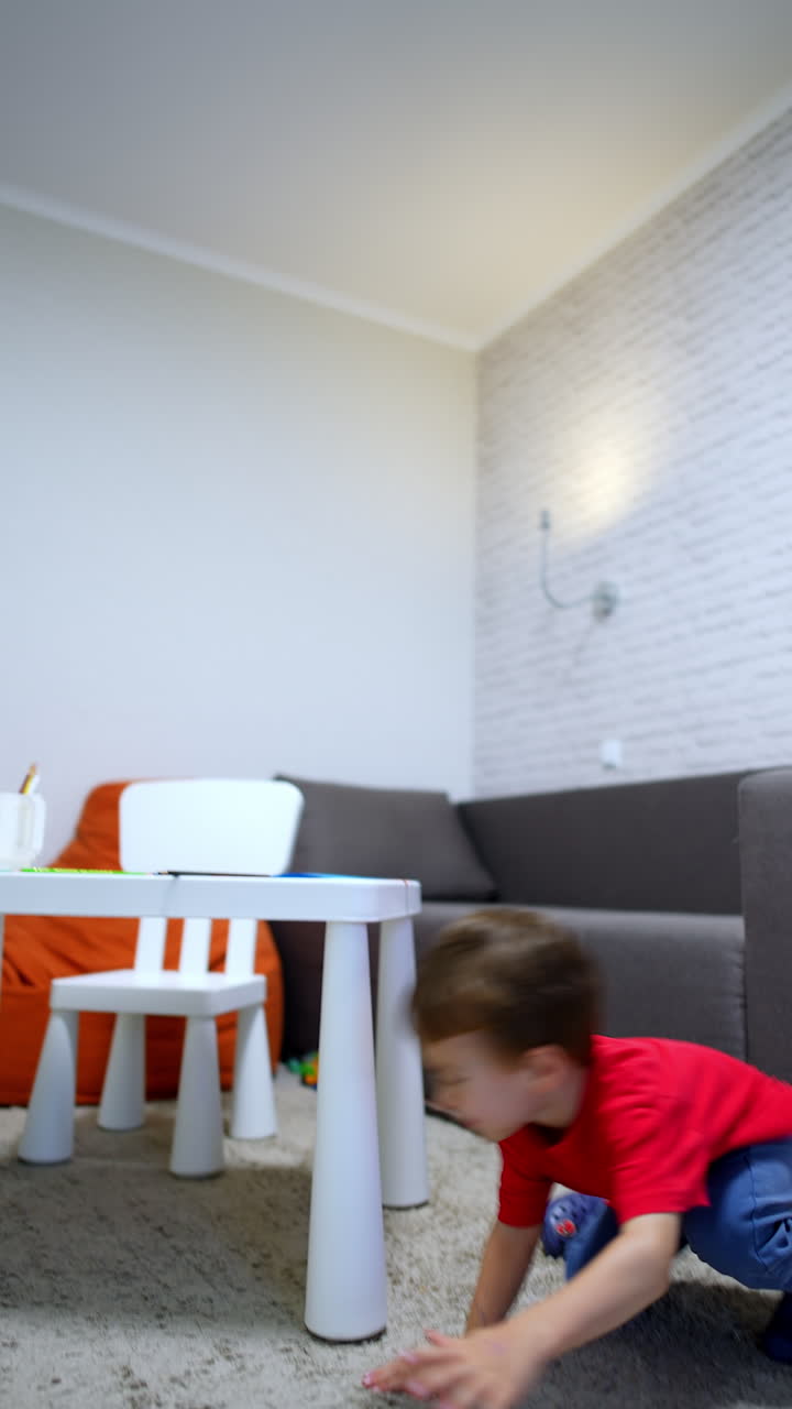 Small kid tumbles on a big sofa. Toddler crawls under the desk to hide. Black cat sits at foreground. Vertical video.