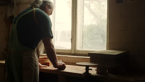 Serious-man-preparing-for-handicraft-lesson-in-studio.-Ceramist-sculpting-clay