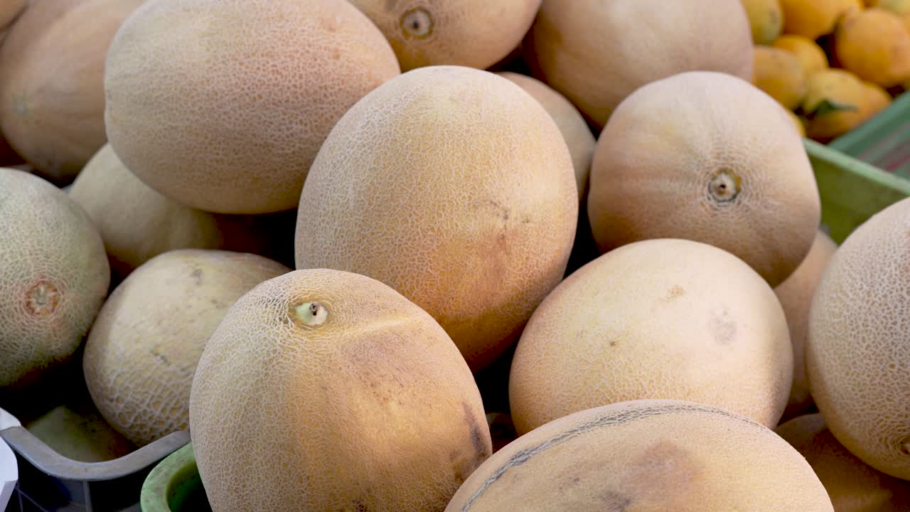 At a lively market, vibrant melons and oranges catch the eye under the warm sun. Shoppers browse, selecting the best fruits for their summer gatherings and refreshing treats