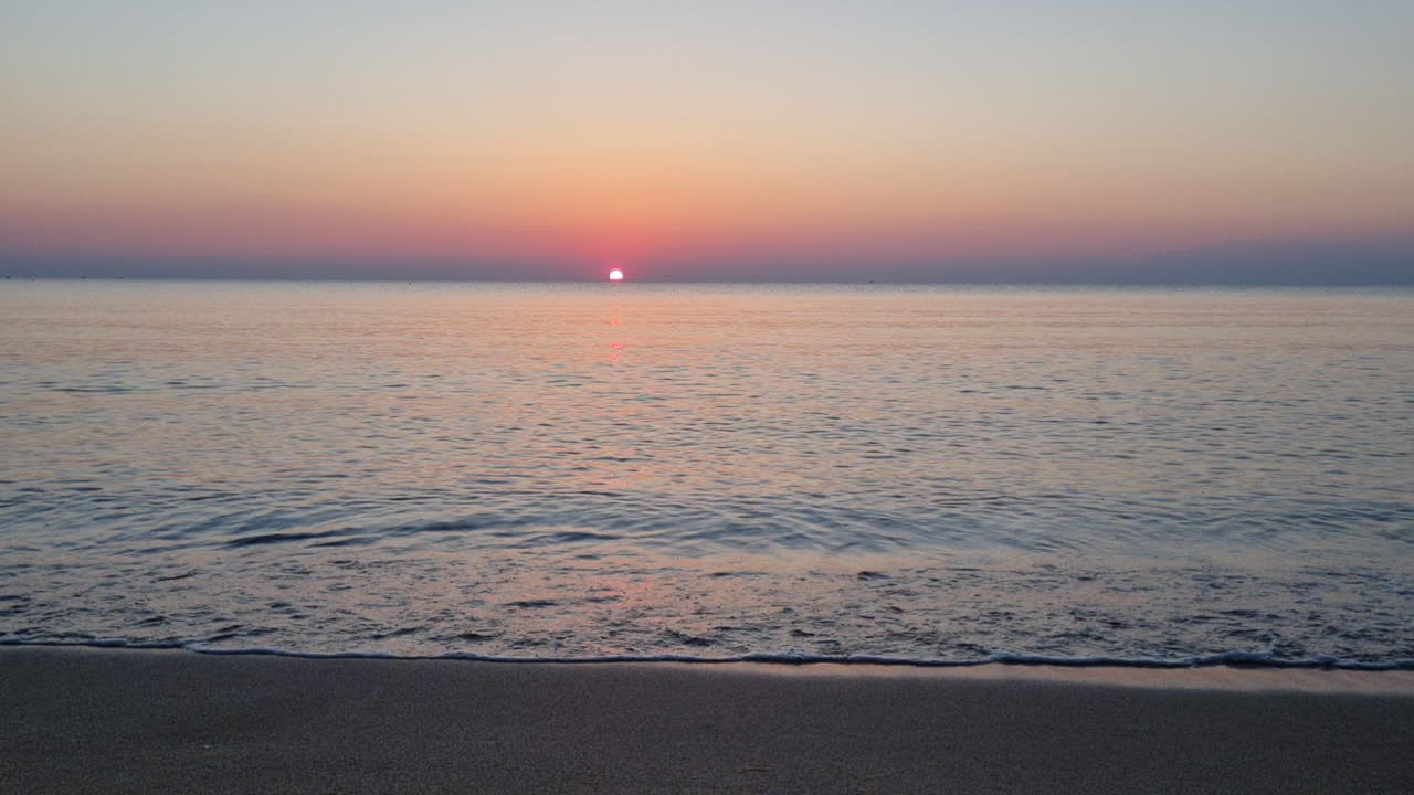 잔잔한 물 표면과 바다 파도가 일출에 모래 해변에 튀다