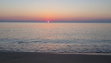 calm water surface and sea waves splash on sandy beach at sunrise