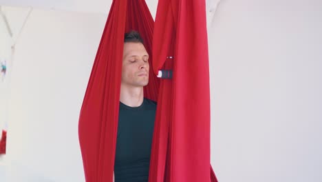 young-man-sits-in-yoga-hammock-and-relaxes-with-closed-eyes
