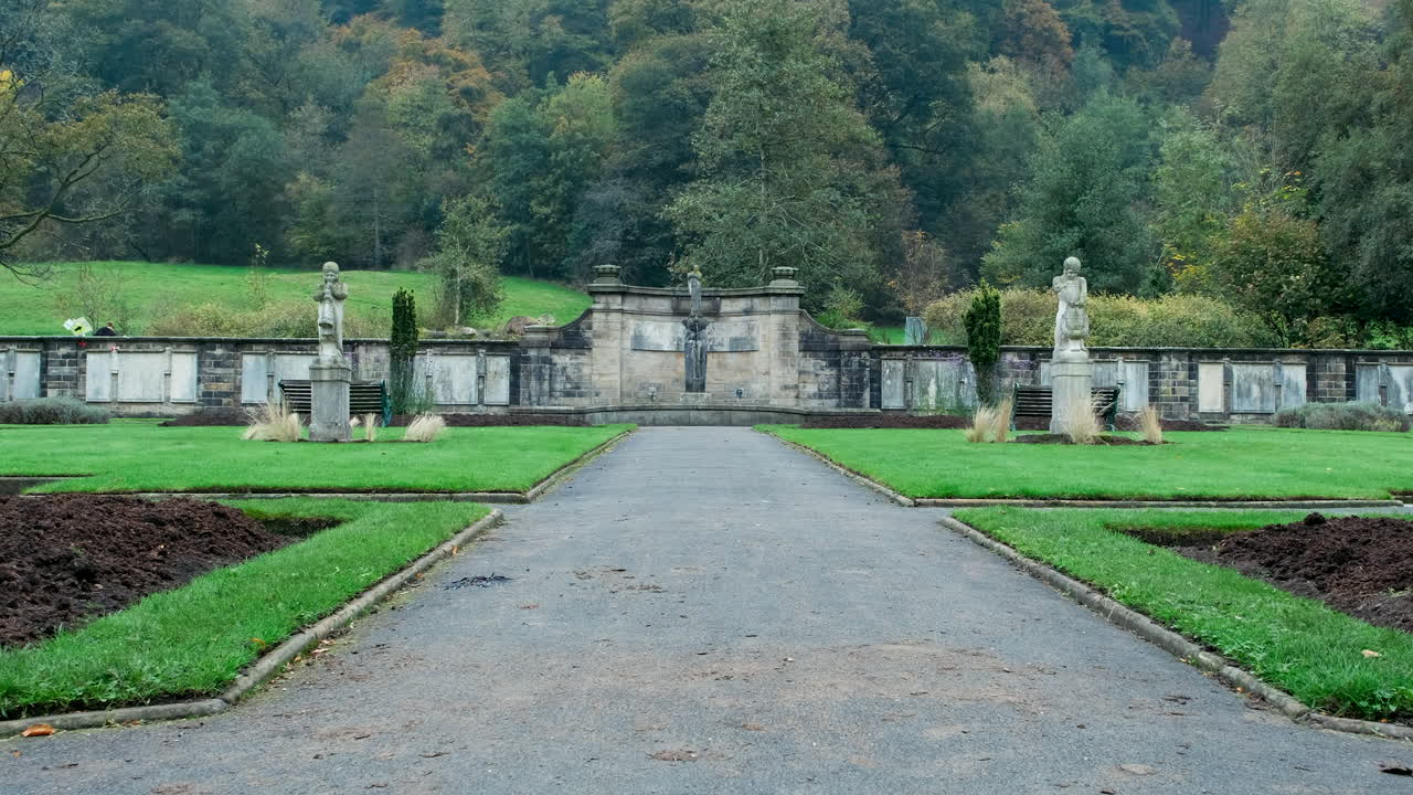 Low symmetrical shot of a man walking his dog through an autumn war memorial garden