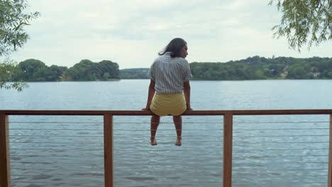 mujer joven sentada sola en paz en la barandilla del muelle junto al estanque disfrutando de las vistas de las aguas tranquilas