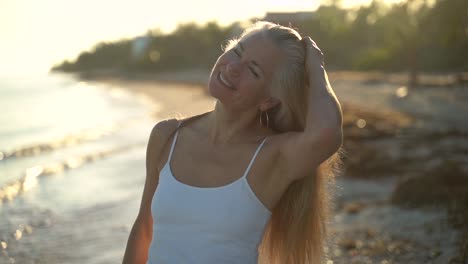 slow motion of mature woman backlit on beach swinging her hair back into the air and eventually looking and smiling at camera