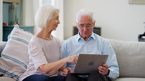 senior couple sitting on sofa using laptop at home together