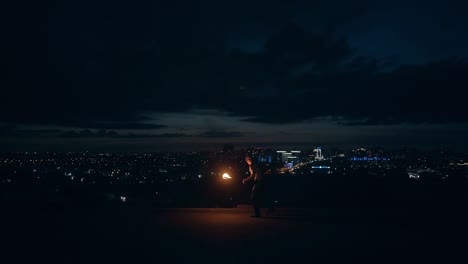 young blond male does tricks with fire breaths fire at night with city skyline in the background