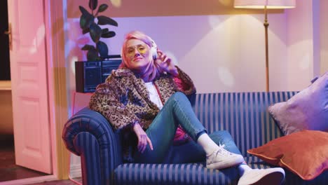 beautiful young caucasian woman in sunglasses and listening to the music sitting on sofa in vintage room at home