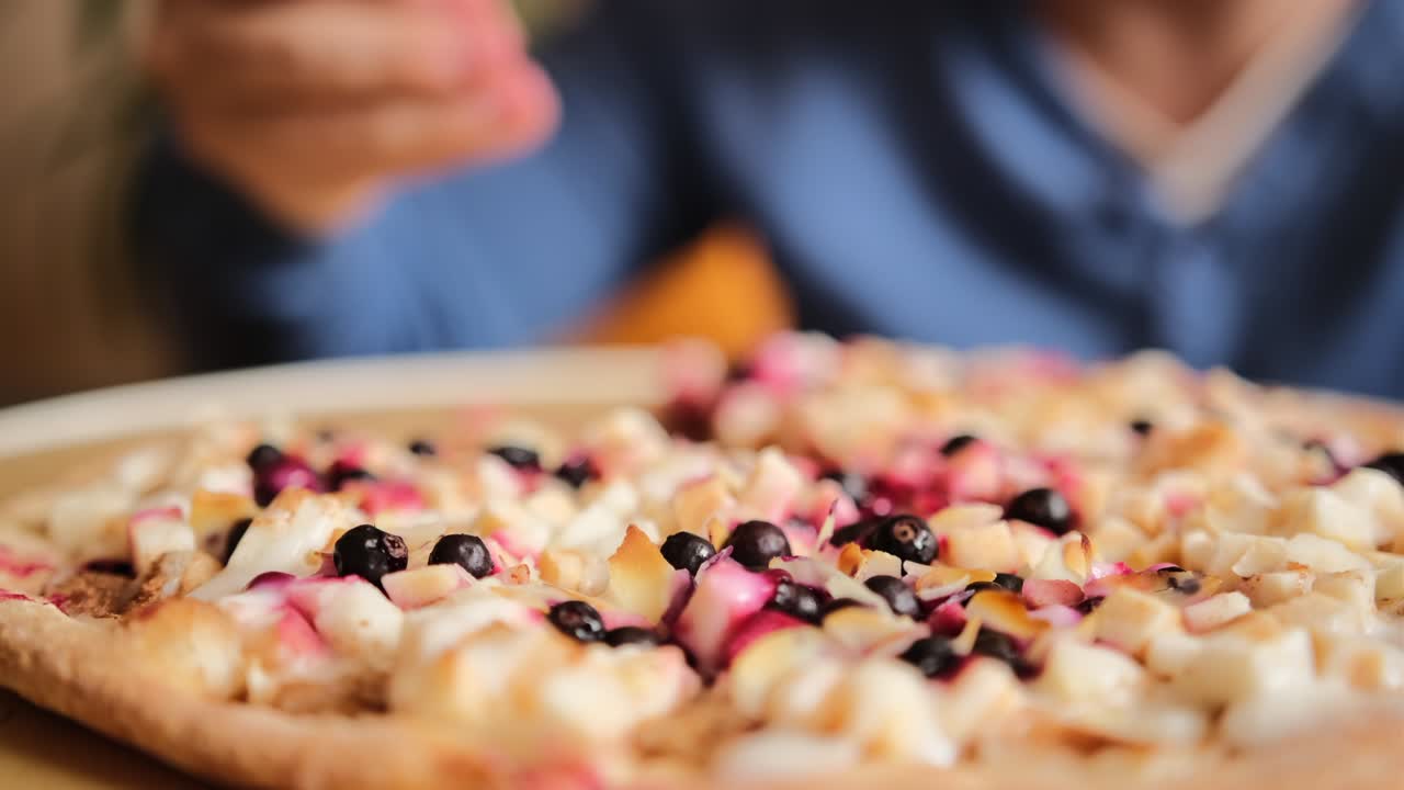 Il ragazzo prende fette di pizza dolce con pezzi di mela, frutti di bosco, scaglie di mandorle e latte condensato