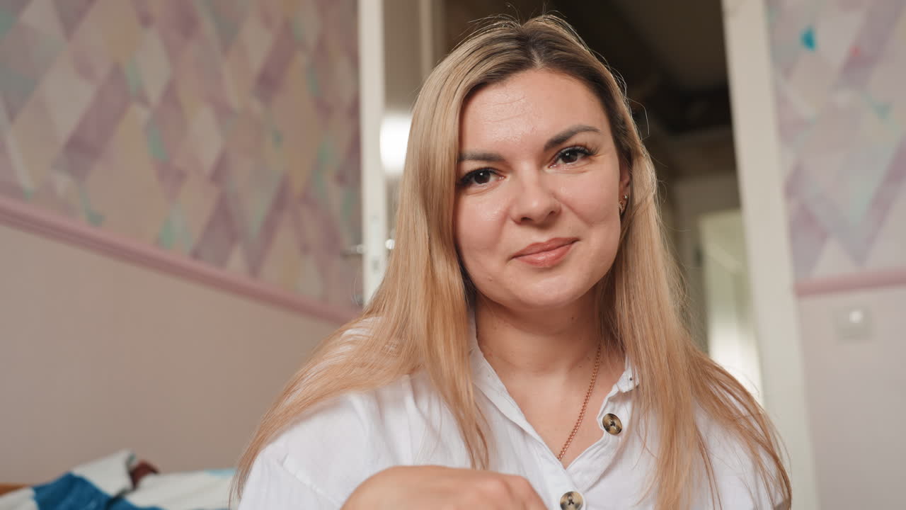 Mor i soveværelset, roligt smil, blødt pastelfarvet tapet, afslappet holdning, direkte øjenkontakt, blide nik, intimt moderligt øjeblik, mor deler beroligelse ved sengetid, subtilt naturligt lys, hyggeligt sengetøj.