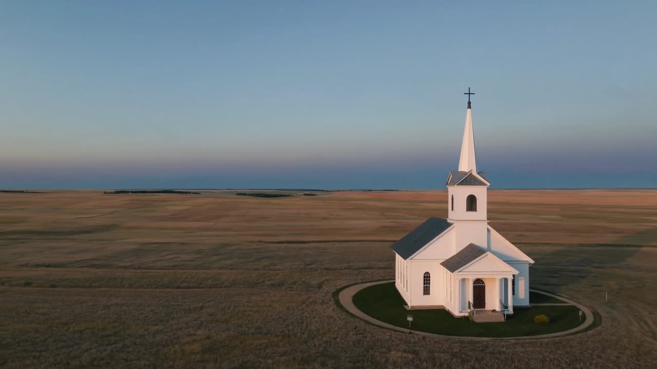 White church stands prominently in golden fields, captured from above, showcasing serene landscape and architectural beauty during twilight, creating a peaceful ambiance