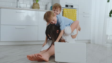 Mamá-Y-Dos-Niños-Juegan-Sentados-En-El-Suelo-Abrazándose-Y-Divirtiéndose.-Una-Familia-Feliz.-El-Juego-Después-De-Ver-La-Computadora-Portátil.-Juegos-Con-Niños.