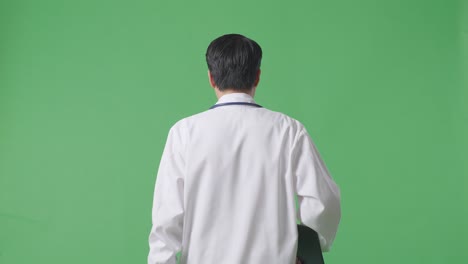 back view of asian male doctor with stethoscope holding a tablet while walking on green screen background in the hospital