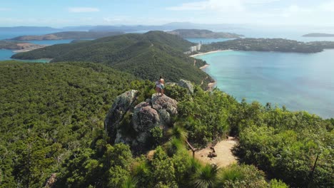 4k drone view flying around a couple standing on a rock at passage peak, a 360-degree panoramic viewpoint on hamilton island in the whitsundays in queensland, australia