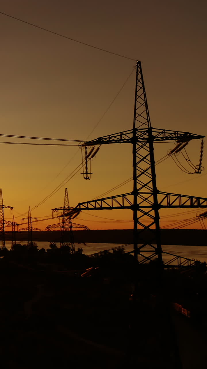 Transmission lines at sunset. High-voltage electric towers near the industrial factory with smoking pipes in the evening. Motion camera top down. Vertical video