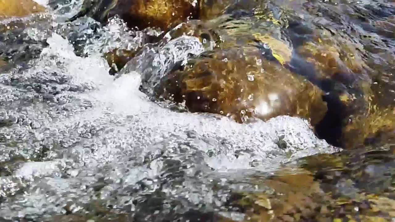 Primo piano al rallentatore di acqua fresca che scorre sulle rocce in un piccolo ruscello **in Marocco**. La scena naturale del ruscello cattura il movimento della corrente limpida