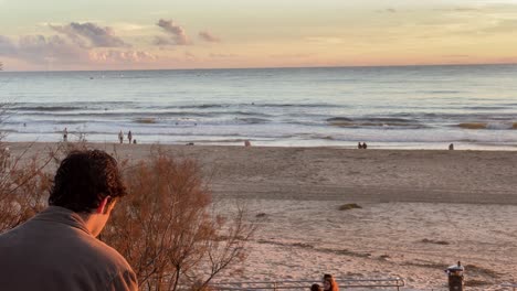 Hombre-Triste-Fumando-Y-Mirando-El-Mar-Al-Atardecer,-Vista-Desde-Atrás